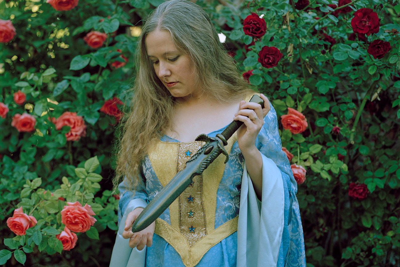 Portrait of Woman in Medieval Costume Blue Dress Holding Large Dagger by Rose Bush in Utah